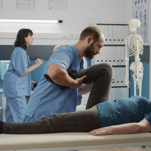 Physician doing legs raise exercise to stretch legs for old patient with mechanical disorders in rehabilitation cabinet. Osteopathy specialist doing physical therapy procedure to cure woman.